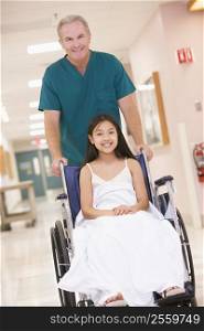 An Orderly Pushing A Little Girl In A Wheelchair Down A Hospital Corridor