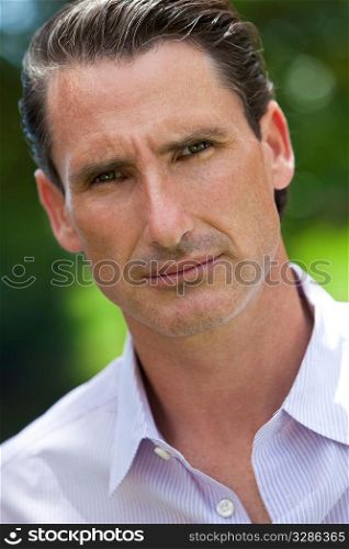 An outdoor portrait of handsome middle aged man shot with sunlight against a natural green background