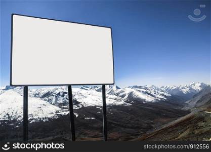 An outdoor white blank billboard with a view of clear blue sky and snow capped mountain range in the background. Karakoram highway, Barbusar Pass. Gilgit Baltistan, Pakistan.