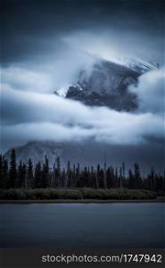 An overcast and moody sunrise obscures Mount Rundle in the distance at Vermilion Lakes in Banff National Park, Canada.