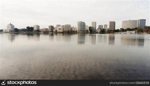 An overcast sky is reflected in the smooth water of Lake Merritt in front of Oakland and an approaching kayaker