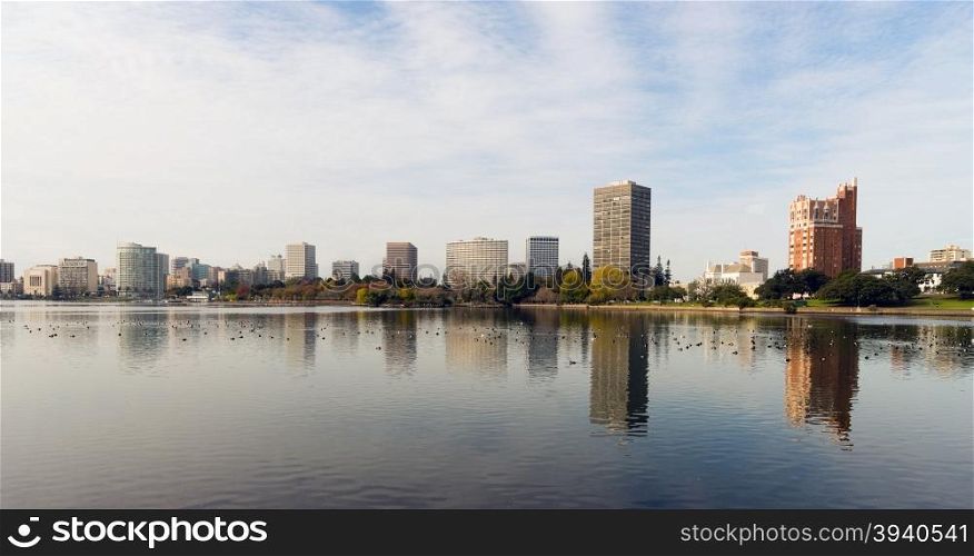 An overcast sky is reflected in the smooth water of Lake Merritt in front of Oakland