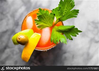 An overhead shot of a lime, lemon, olive, and parsley garnished Bloody Mary on a grey marble counter top.