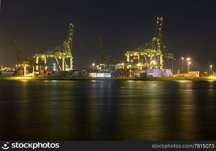 An overview of the Rotterdam Container harbor, with its huge cranes, stacked containers and industrial activity at night. Business continues 24/7