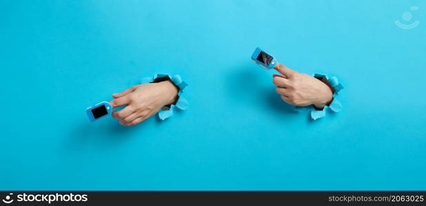 an oximeter for measuring oxygen in the blood is worn on the index finger, part of the hand is sticking out of a torn hole in the blue paper