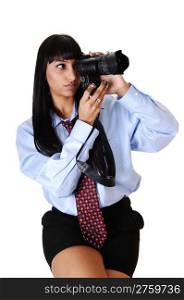 An pretty young woman with a dELS camera taking some pictures, in blackshorts and a blue shirt and tie, sitting, over white background.