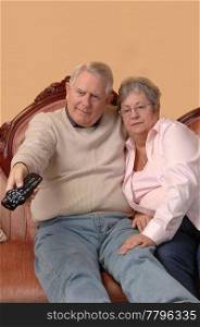 An senior couple sitting on the sofa in there living room and switchingchannels on the TV, for white background.