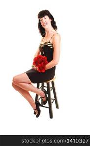 An tall young woman in a black dress sitting on a chair with red roses inher hand in the studio for white background.
