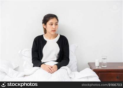 An uncomfortable woman sits on the bed and has medicine on the table.