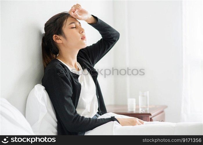 An uncomfortable woman sits on the bed and has medicine on the table.