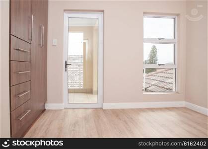 An unfurnished bedroom on the first floor with glass doors leading to balcony, build in cupboards, and laminated floor, of a newly build house.