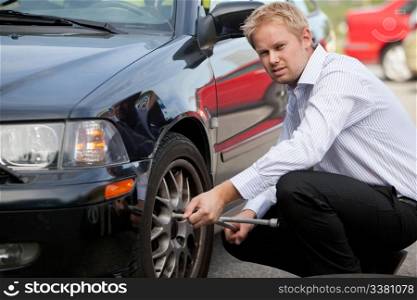 An unhappy business man changing a tire on the road