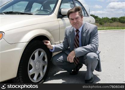 An unhappy looking businessman discovering a screw in his flat tire.