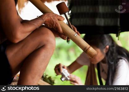 An unidentified old Lavae tribe man smoking a traditional tobacco bamboo bong while a female tourist visiting a village. Bolaven, Laos. Focus on bong.