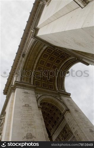 An upward view of the Arc de triomphe, the famous landmark and monument for the unknown soldier on the Champs Elisee in Paris, France on a cloudy day
