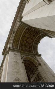 An upward view of the Arc de triomphe, the famous landmark and monument for the unknown soldier on the Champs Elisee in Paris, France on a cloudy day