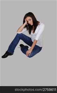An young pretty woman in jeans and black boots, smiling and sittingon the floor, for light gray background.
