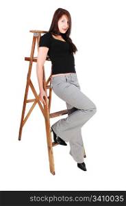 An young woman sitting on the step of a stepladder in a gray dress pantsand black sweater, shooing her fantastic body.