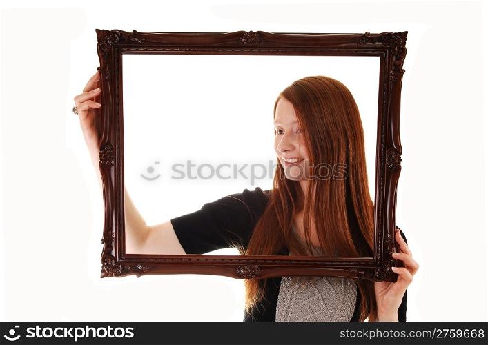 An young woman with long red hair holding a picture frame, in a blackdress, with empty copy space in the frame, on white background.