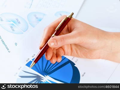 Analyzing report. Close up of male hand holding pen and pointing at graphs