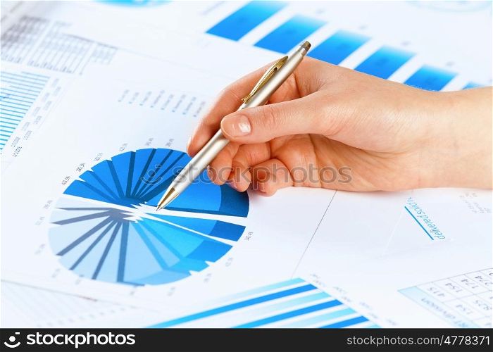 Analyzing report. Close up of male hand holding pen and pointing at graphs