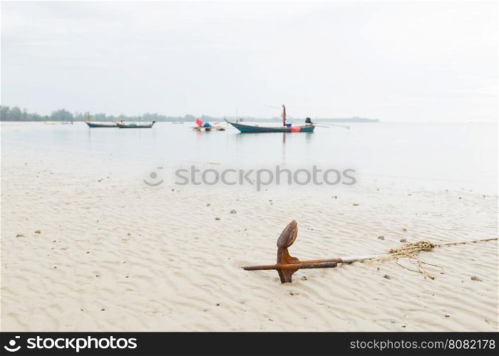 Anchor resting on the beach. Small fishing boat moored at sea.