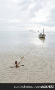 Anchor resting on the beach. Small fishing boat moored at sea.