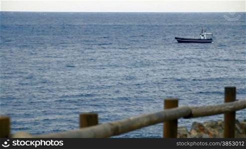 Anchored boat in the Mediterranean Sea.View from the seashore with a wooden balustrade out of focus.