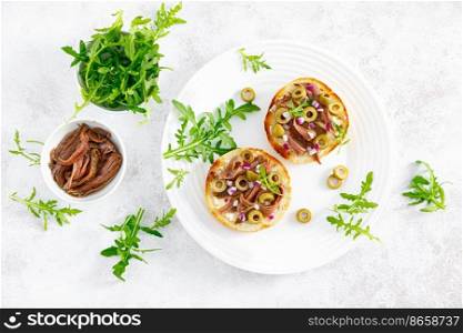 Anchovy toasts with olives and arugula. Top view