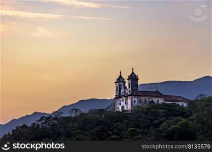 Ancient and historic church on top of the hill during sunset in the city of Ouro Preto in Minas Gerais, Brazil with the mountains behind at Ouro Preto city. Ancient and historic church on top of the hill during sunset at Ouro Preto city