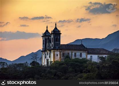 Ancient and historic church on top of the hill during sunset in the city of Ouro Preto in Minas Gerais, Brazil with the mountains behind. Ancient and historic church on top of the hill during sunset