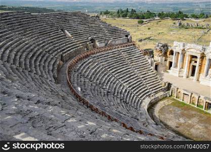 Ancient antique amphitheater in the city of Hierapolis in Turkey. Steps and antique statues with columns in the amphitheater. Ancient antique amphitheater in city of Hierapolis in Turkey. Steps and antique statues with columns in the amphitheater