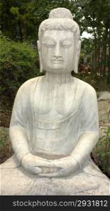 Ancient Buddha stone statue against green woods