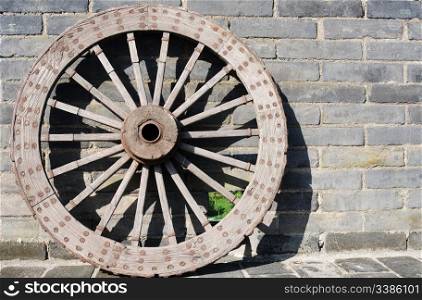 Ancient carriage wheel against brick wall