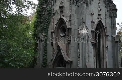 Ancient crypt covered with ivy plant in graveyard cemetery. Old gothic crypt with statue of gaurdian angel on the top against cloudy sky background