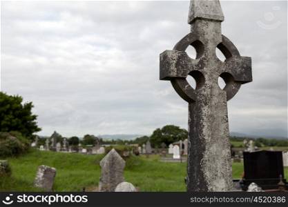ancient monument and burial concept - old grave cross, headstones and ruins on celtic cemetery graveyard in ireland