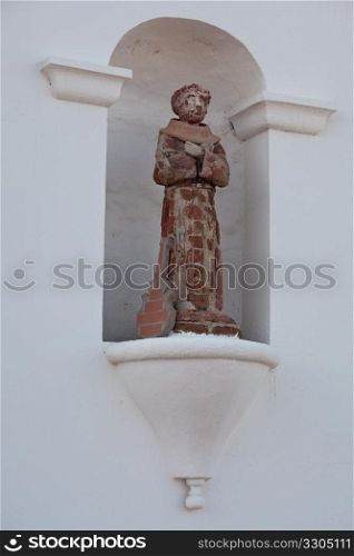 Ancient tile and plaster saint with a guitar leaning against the legs of the statue in Mission near Oceanside