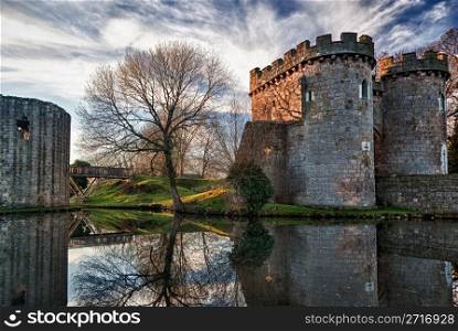 Ancient Whittington Castle in Shropshire, England reflecting in a calm moat round the stone buildings and processed in HDR