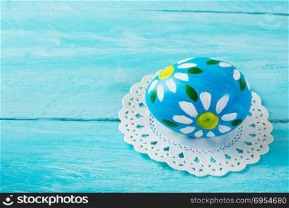 ??and-painted blue Easter egg with floral design on a blue wood plank background. Easter background. Easter symbol. Copy space