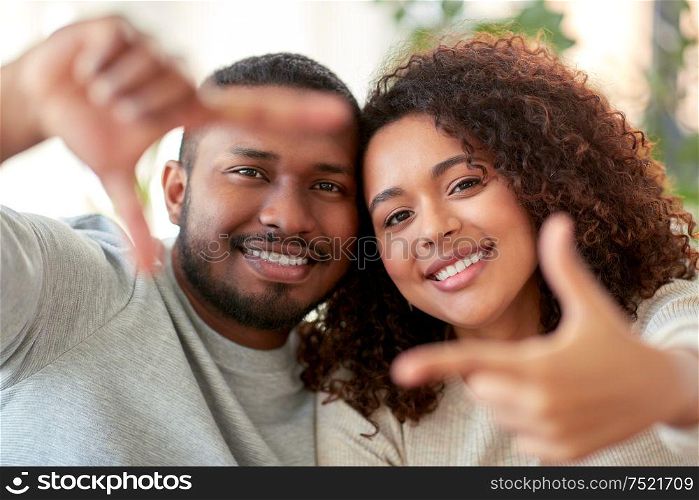 and people concept - happy african american couple making selfie or viewfinder gesture at home. happy couple making selfie gesture at home
