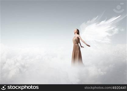 Angel girl flying high. Attractive woman with angel wings on sky background