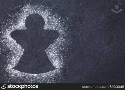 Angel shape formed by powdered sugar on slate, Christmas concept with copy space on the side. Angel