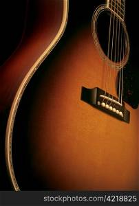 Angle shot of a maple wood acoustic guitar showing wood grain, bridge and strings.