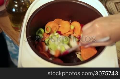 Angle view of woman hands stirring slowly vegetables in multicooker ,while cooking soup in the kitchen