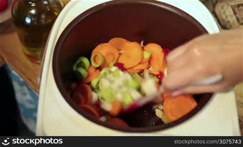Angle view of woman hands stirring slowly vegetables in multicooker ,while cooking soup in the kitchen