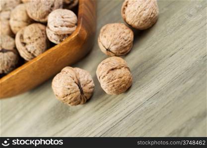 Angled horizontal photo of whole walnuts lying on faded wood with additional nuts and wooden bowl in background