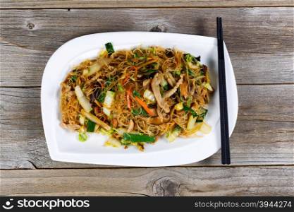 Angled view of cooked chicken strips and rice noodles with vegetables on rustic wood setting.