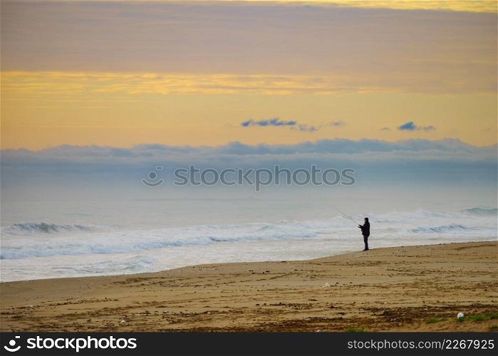 Angler with fishing rod on sea shore at morning. Spain Costa Blanca.. Angler with fishing rod on sea shore