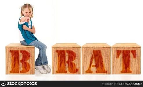 Angry american 7 year old girl sitting on blocks spelling the word brat over white background.