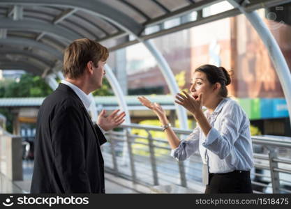 Angry American Businessman and businesswoman secretary in formal suits argue by raising their arms and shouting outside office. Couple argument in town. Husband and wife family marriage conflict.